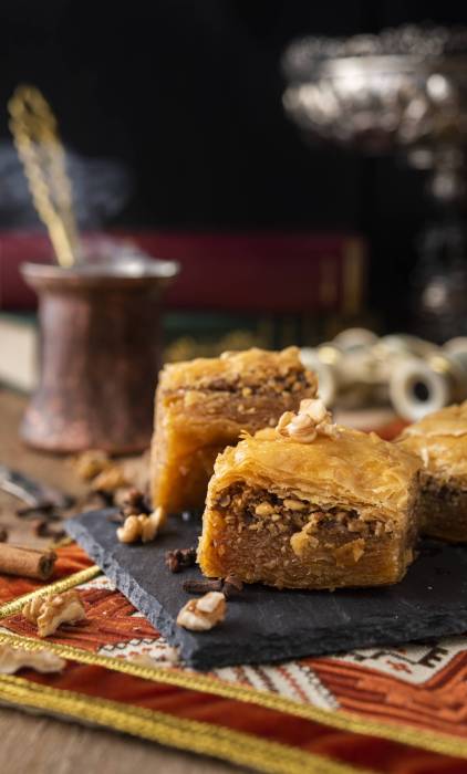 Baklava sweets with nuts on it with coffee and cinnamon Baklava sweets on a black stone with coffee and books, binoculars at the back